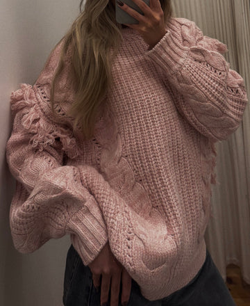 Person wearing a pink knitted sweater taking a mirror selfie.