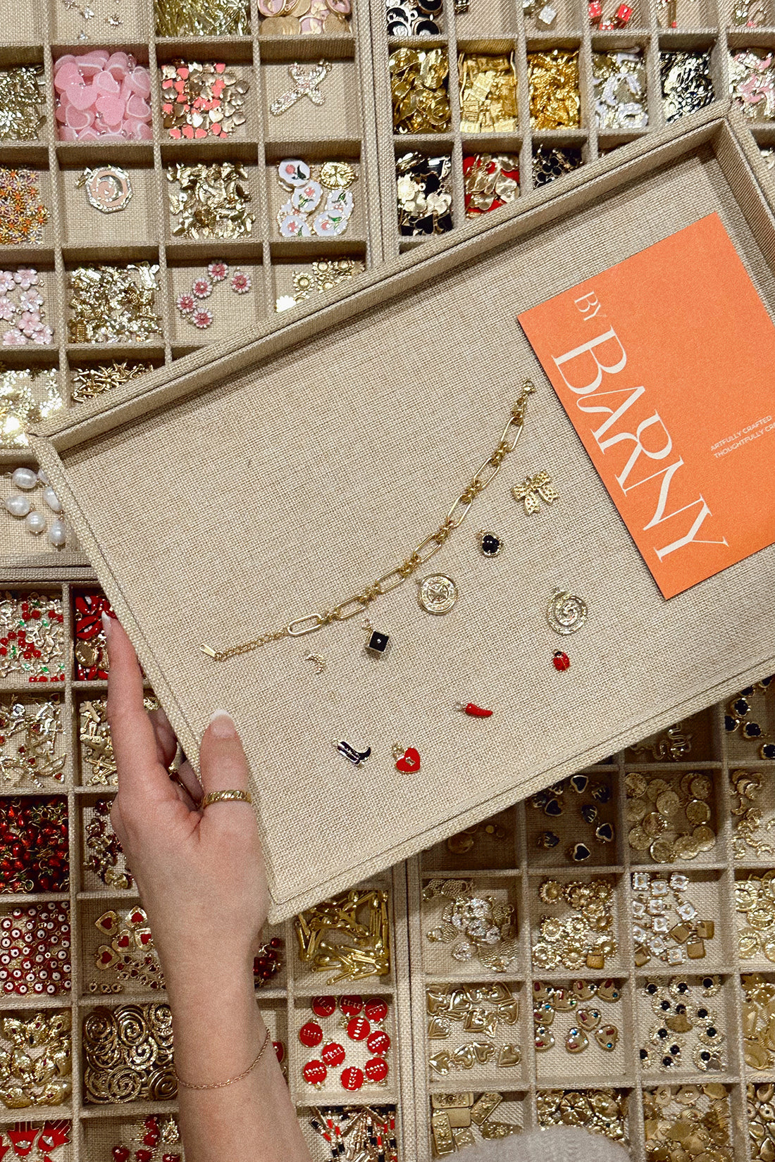 A person holding a Charm Jewellery designed board in front of a display case containing various charms.