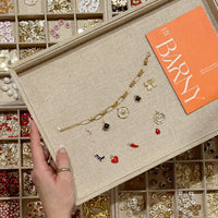 A person holding a Charm Jewellery designed board in front of a display case containing various charms.
